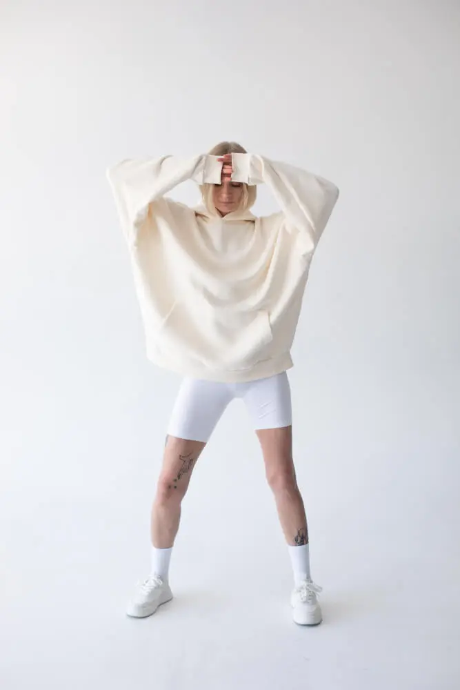 Bella mujer rubia posando con sudadera blanca y leggings posando contra un fondo blanco
